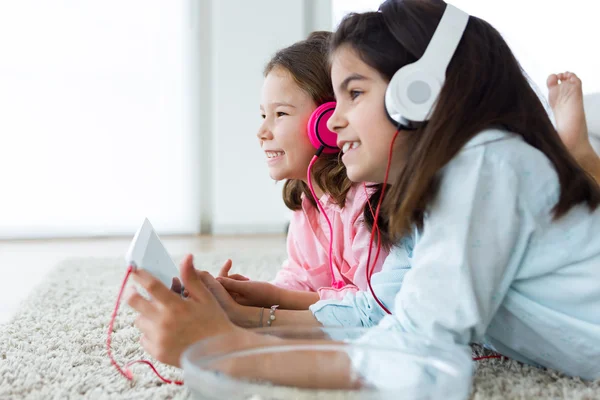 Schöne junge Schwestern hören Musik mit digitalem Tablet. — Stockfoto