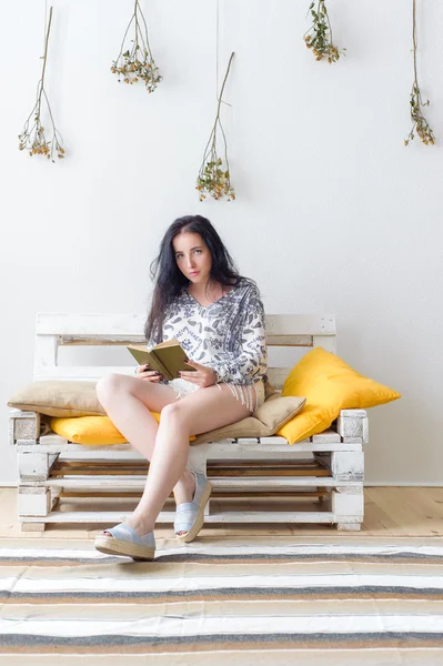 Evdeki kanepede oturup kitap okuyan rahat, mutlu bir kadın.