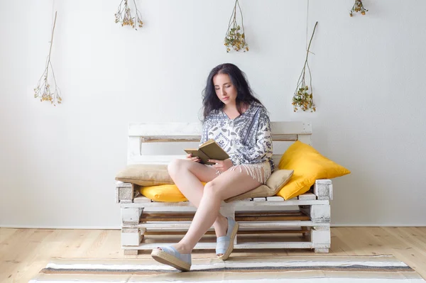 Evdeki kanepede oturup kitap okuyan rahat, mutlu bir kadın.