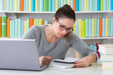 Kadın kütüphanede kitap okuyor.