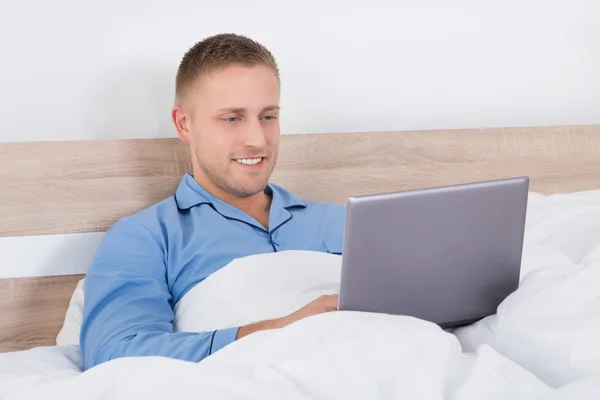Junger Mann benutzt Laptop auf Bett — Stockfoto