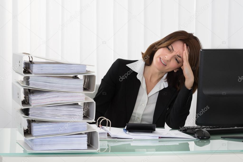 Stressed Businesswoman Looking At Stack Of Folders