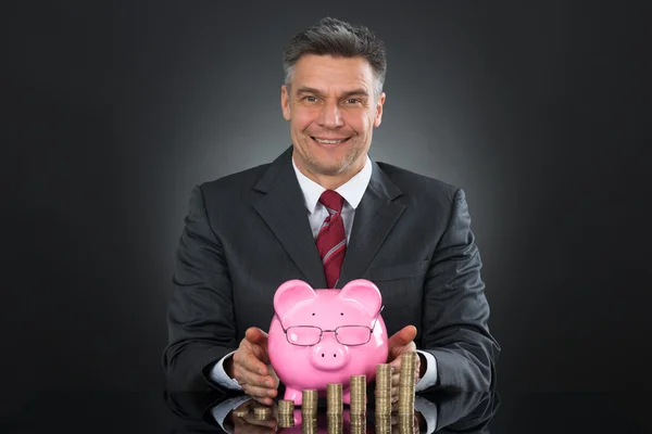 Бизнесмен с монетами и свиньёй — стоковое фото