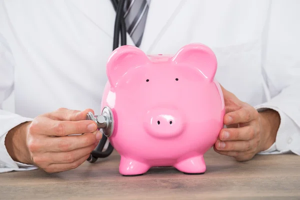 Médico mão examinando Piggybank com estetoscópio — Fotografia de Stock