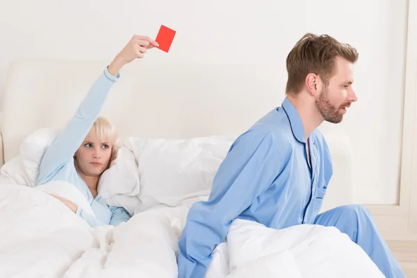 Mujer mostrando tarjeta roja al hombre en la cama — Foto de Stock