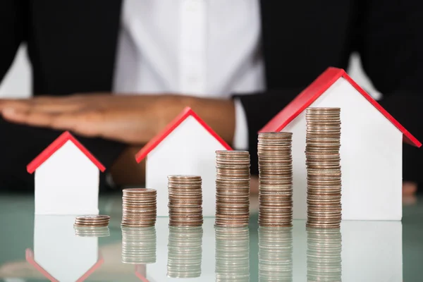 Mujer de negocios con modelos de casa y monedas — Foto de Stock