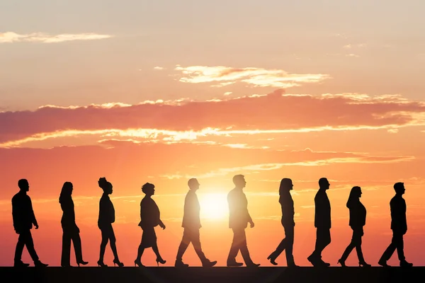 Silhuetas de pessoas caminhando ao pôr do sol — Fotografia de Stock