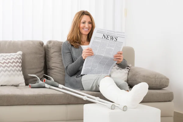 Femme avec jambe fracturée lecture journal — Photo