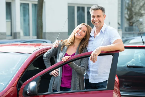 Счастливая пара с новым красным автомобилем — стоковое фото