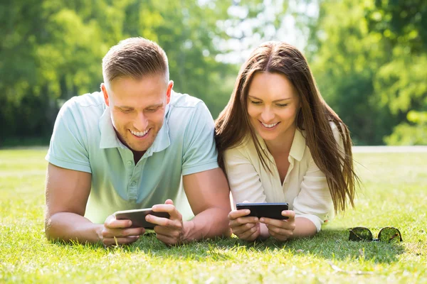 Jeune couple regardant leurs téléphones mobiles — Photo