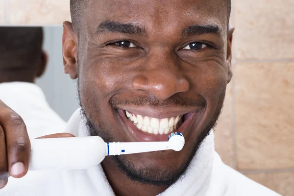 Africano hombre limpieza su dientes en frente de espejo —  Fotos de Stock