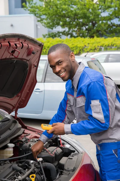 Mécanicien utilisant le multimètre pour vérifier la batterie de voiture — Photo