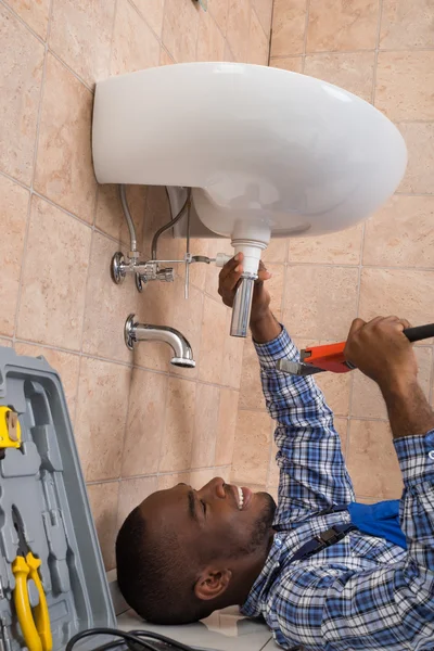 Loodgieter liggend op vloer tot vaststelling van de wastafel In de badkamer — Stockfoto