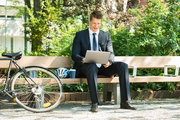 Empresário sentado no banco usando laptop — Fotografia de Stock