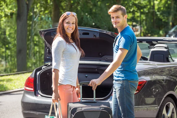 Coppia sorridente che mette il bagaglio in un bagagliaio dell'automobile — Foto Stock