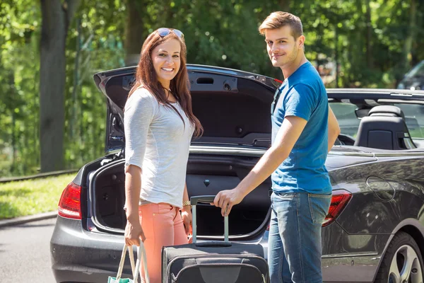 Lachende paar plaatsen van bagage In de kofferbak van een auto — Stockfoto