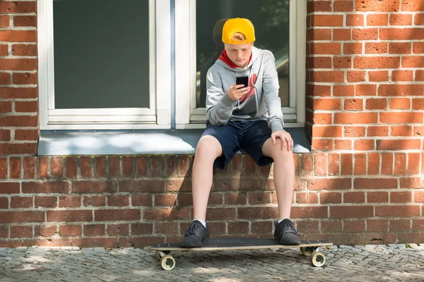 Pojke med Skateboard använda på sin mobiltelefon — Stockfoto