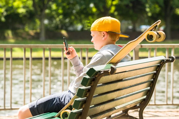 Garçon assis sur le banc en utilisant un téléphone mobile — Photo