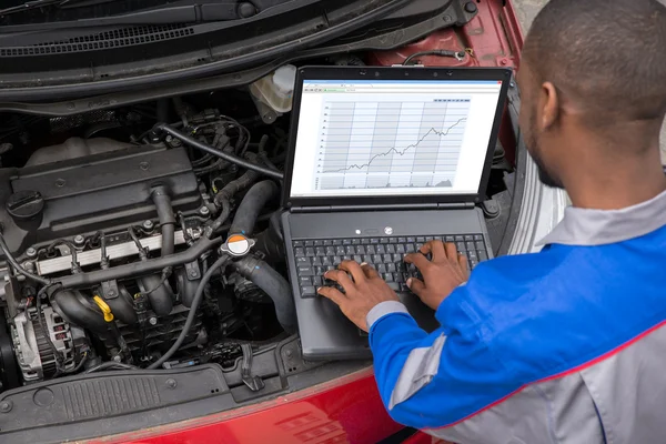 Mecânico com laptop enquanto examina o motor — Fotografia de Stock