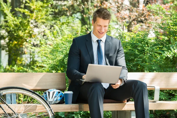 Uomo d'affari seduto sul banco utilizzando il computer portatile — Foto Stock