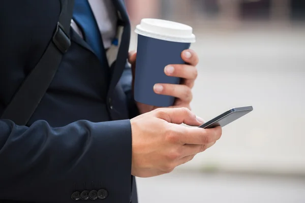 Рука бизнесмена с мобильным телефоном и кофейной чашкой — стоковое фото
