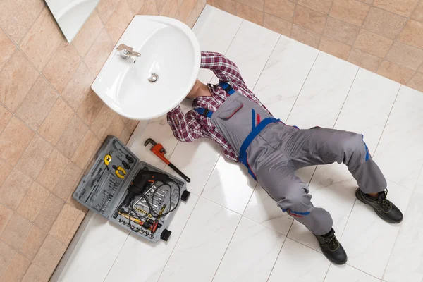 Plombier mâle couché sur le plancher de réparation évier dans la salle de bain — Photo