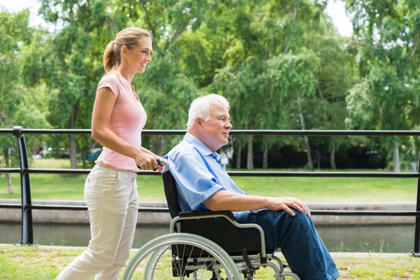 Lächelnde junge Frau hilft ihrem behinderten Vater im Rollstuhl — Stockfoto