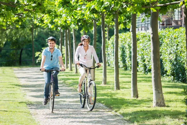 Couple souriant chevauchant sur des vélos dans le parc — Photo