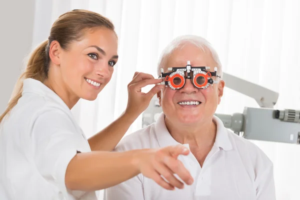 Optometrista femenina verificando la visión del paciente con marco de prueba —  Fotos de Stock