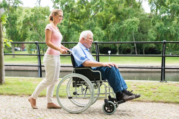 Sorridente giovane donna che assiste il padre disabile sulla sedia a rotelle — Foto Stock