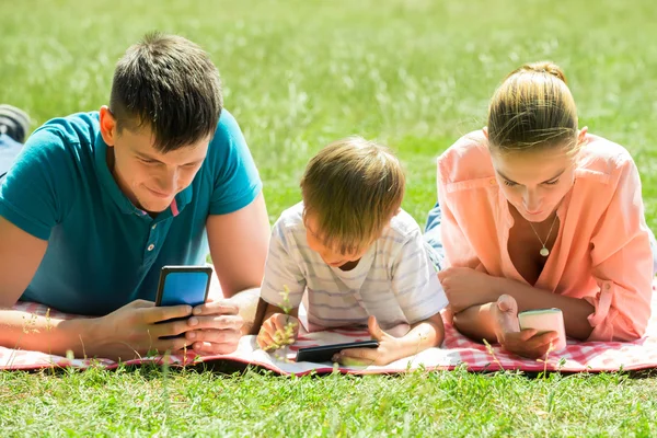 Familie legt sich mit ihren Smartphones in den Park — Stockfoto