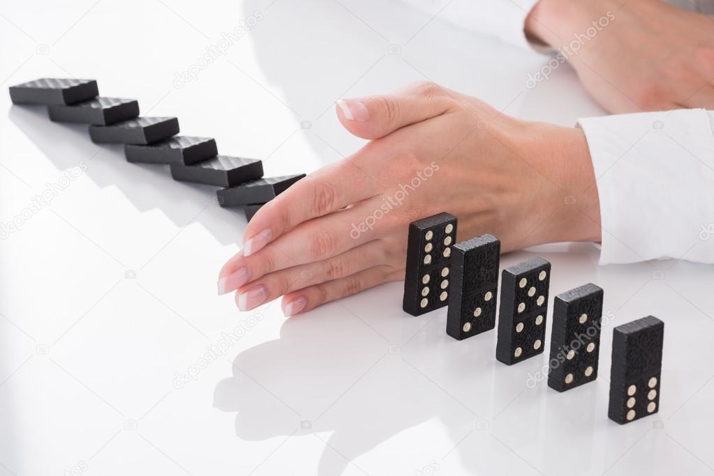 Person's Hand Stopping Dominos Falling On Desk