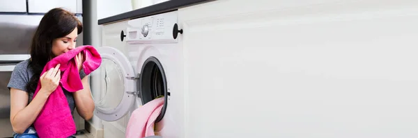 Woman Smelling Cleaned Clothes Near The Electronic Washer At Laundry Room