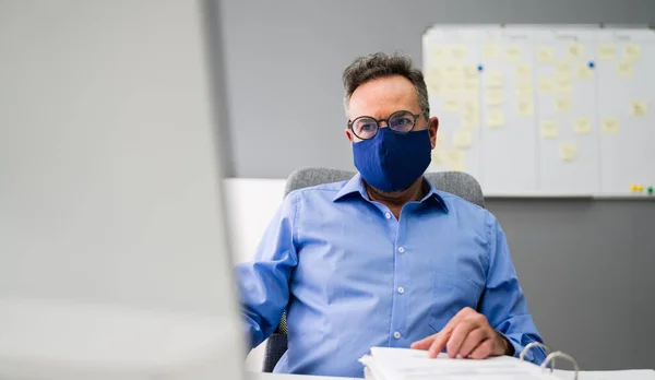 Elder Business Employee Working At Computer Wearing Facial Mask