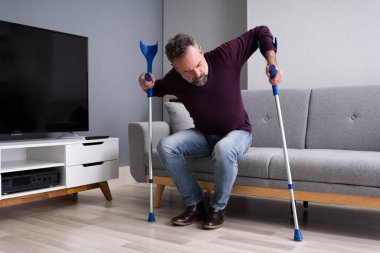 Koltuk değneklerini kullanarak kazadan sonra bacağı kırılan adam.