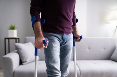 Yaşlı adam halıda yürümek için koltuk değneklerini kullanıyor.