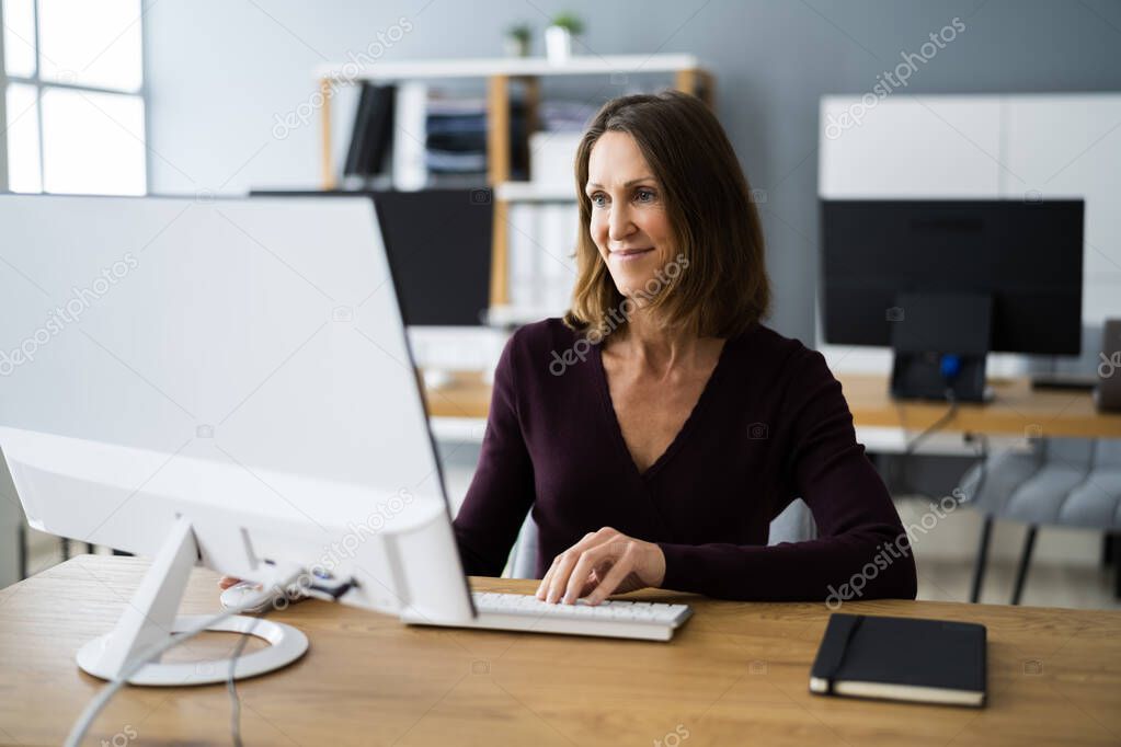 Woman In Office Using Business Computer At Desk