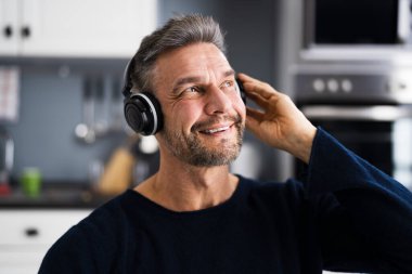 Gülümseyen yaşlı adam kulaklıkla müzik dinliyor.