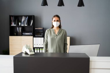 Ofisteki resepsiyonist kadın yüz maskesi takıyor.