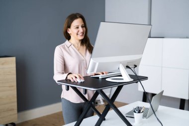 Adjustable Height Desk Stand In Office Using Computer clipart