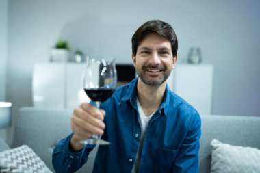 Evdeki video konferansında kırmızı şarap içen adam.