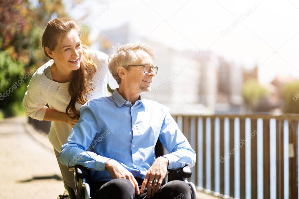 Senior Care And Wheelchair Transport. Smiling Woman Pushing Elderly Man