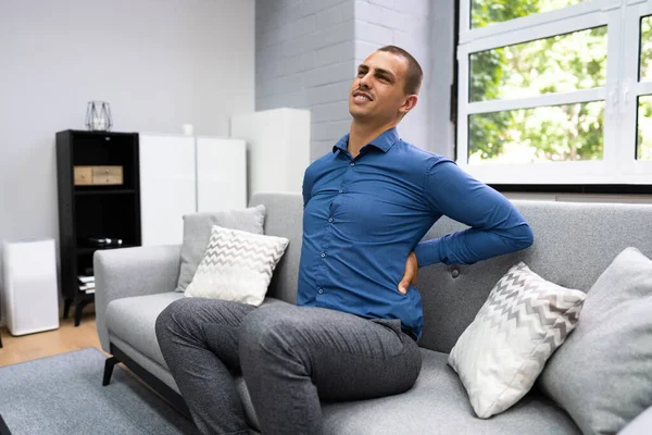 Man Sitting On Sofa Having Back Pain