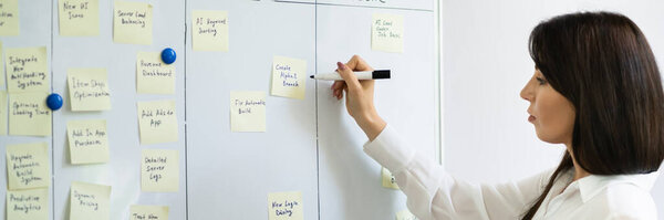 Женщина, пишущая на липких записках на доске проекта Канбан