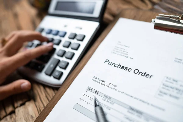 Person Hand Filling A Purchase Order Form On Wooden Desk