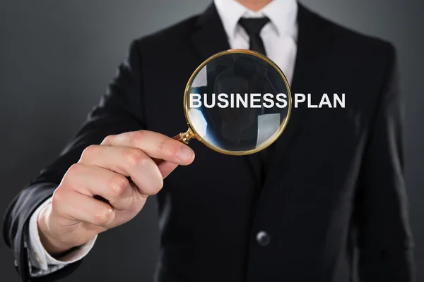 Uomo d'affari che mostra Business Plan attraverso lente di ingrandimento — Foto Stock