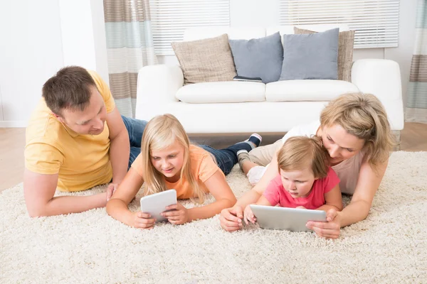 Famiglia utilizzando compresse sdraiato su tappeto — Foto Stock