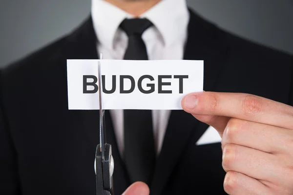 Бизнесмен сокращает бюджет Слова на бумаге ножницами — стоковое фото