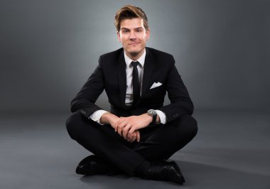 Gri arka plan üzerinde oturan kendine güvenen iş adamı