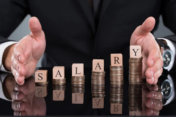 Empresario protegiendo bloques salariales en monedas apiladas —  Fotos de Stock